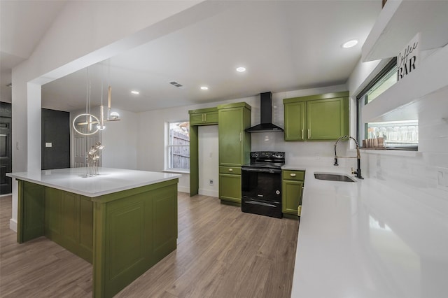 kitchen with light wood finished floors, wall chimney range hood, black range with electric cooktop, green cabinets, and a sink