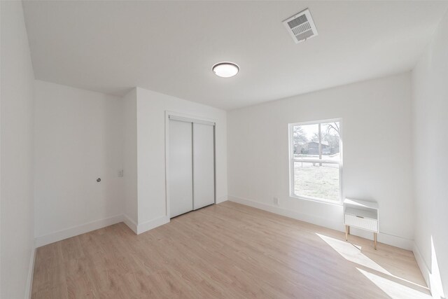 unfurnished bedroom with baseboards, visible vents, light wood-style flooring, heating unit, and a closet