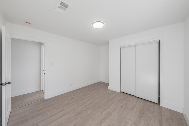 unfurnished bedroom featuring light wood finished floors, baseboards, visible vents, and a closet