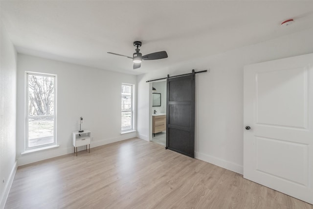 unfurnished bedroom with a barn door, multiple windows, light wood-type flooring, and baseboards