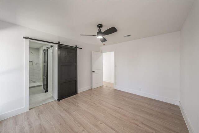 unfurnished bedroom with light wood-type flooring, visible vents, baseboards, and a barn door