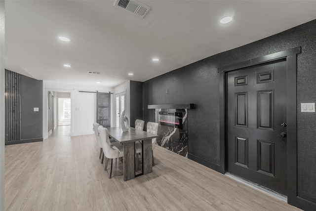 dining space with a textured wall, a barn door, visible vents, baseboards, and light wood-type flooring