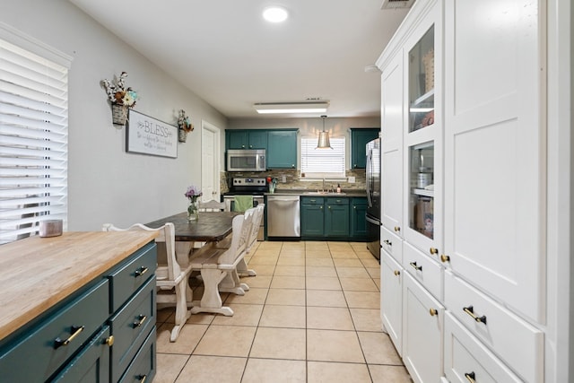 kitchen featuring light tile patterned flooring, stainless steel appliances, a sink, tasteful backsplash, and green cabinetry