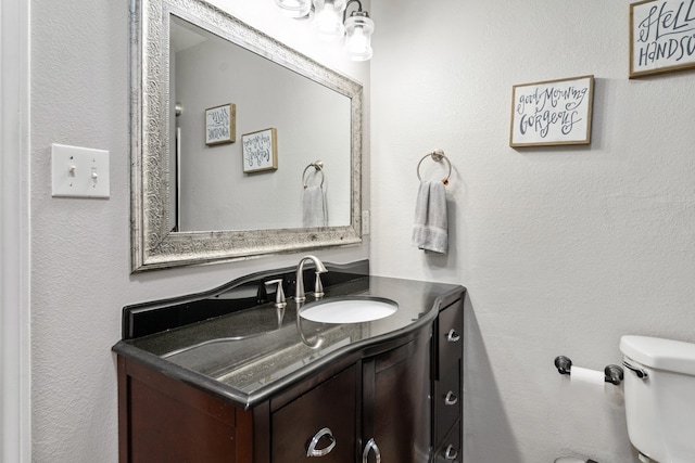 bathroom with toilet, a textured wall, and vanity