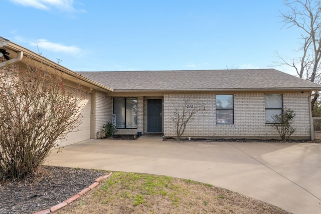 view of front facade with a garage, a shingled roof, concrete driveway, and brick siding