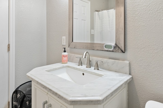 bathroom with a textured wall, vanity, and toilet