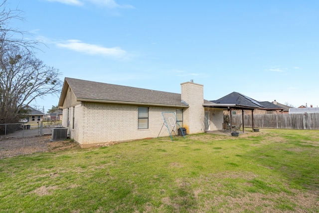 back of property with central air condition unit, a fenced backyard, a chimney, and a lawn