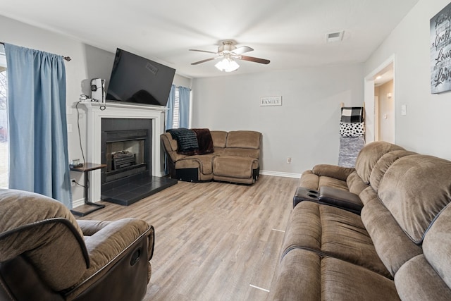 living area featuring a fireplace, light wood finished floors, visible vents, ceiling fan, and baseboards