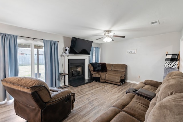 living area with baseboards, visible vents, a ceiling fan, a tile fireplace, and wood finished floors