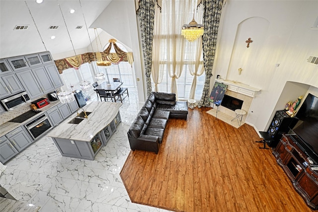 living room featuring high vaulted ceiling, marble finish floor, visible vents, and a tiled fireplace