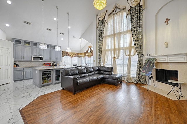 living room with a healthy amount of sunlight, high vaulted ceiling, visible vents, and a tiled fireplace