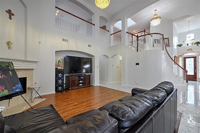 living area with visible vents, stairway, a tiled fireplace, an inviting chandelier, and wood finished floors