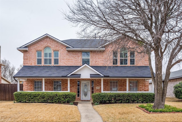 traditional home featuring brick siding, a front lawn, and fence