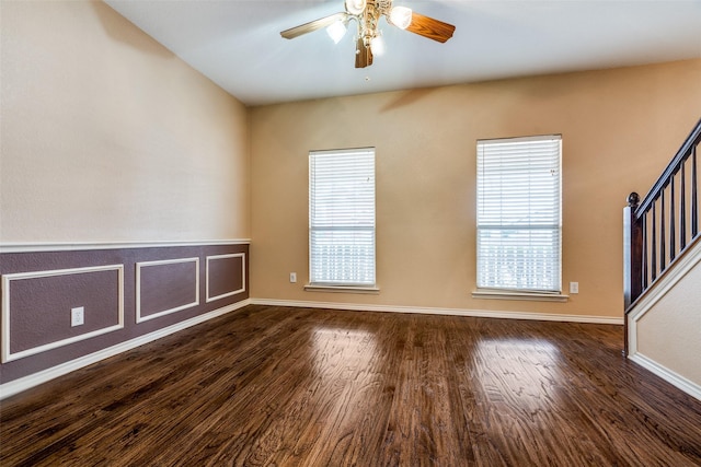 empty room with a ceiling fan, a wealth of natural light, dark wood finished floors, and stairway