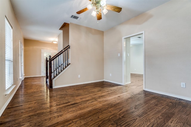 unfurnished room with baseboards, visible vents, dark wood-style floors, ceiling fan, and stairs