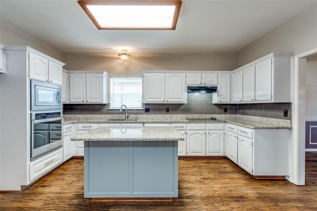 kitchen with white cabinets, dark wood-style floors, stainless steel appliances, under cabinet range hood, and a sink