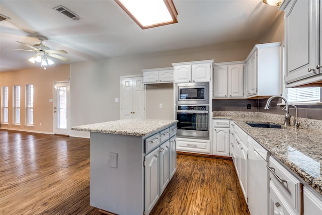 kitchen featuring dark wood-type flooring, a sink, visible vents, appliances with stainless steel finishes, and a center island