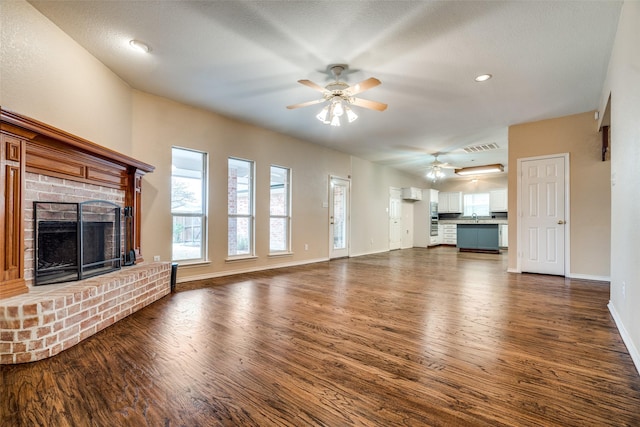 unfurnished living room featuring ceiling fan, dark wood-type flooring, visible vents, baseboards, and a brick fireplace