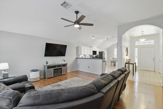 living room featuring visible vents, light wood-type flooring, lofted ceiling, arched walkways, and a ceiling fan