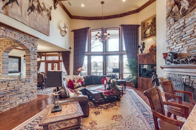 living area featuring crown molding, a fireplace, wood finished floors, a towering ceiling, and an inviting chandelier