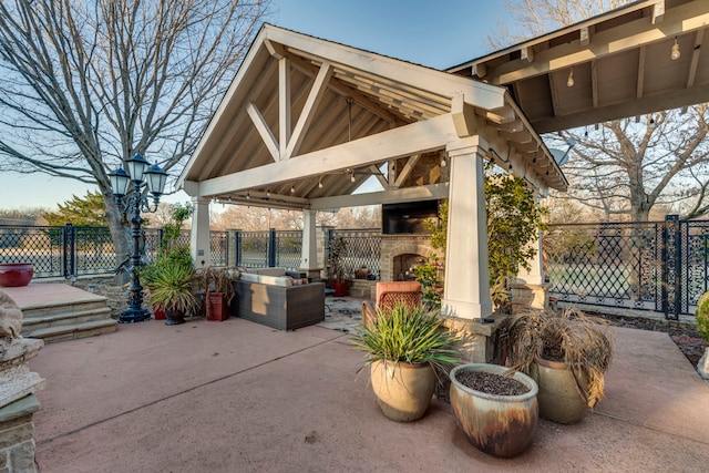 view of patio with an outdoor stone fireplace, fence, and a gazebo