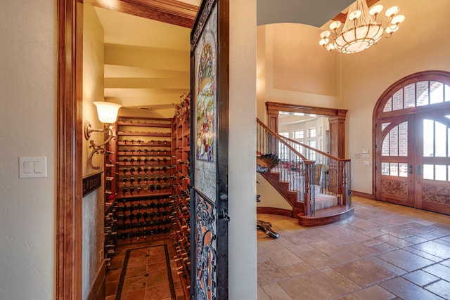 wine cellar with baseboards, a towering ceiling, an inviting chandelier, stone tile flooring, and french doors