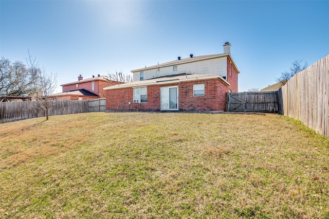 back of house featuring a chimney, brick siding, a lawn, and a fenced backyard