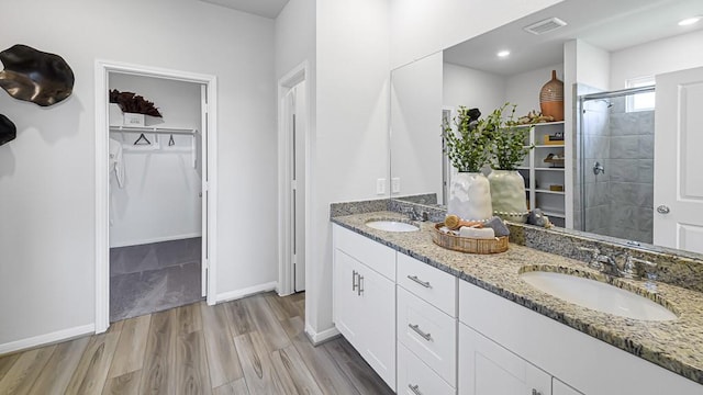 bathroom with a walk in closet, visible vents, a sink, and wood finished floors