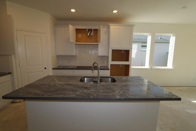 kitchen featuring a center island with sink, dark stone counters, white cabinets, a sink, and recessed lighting