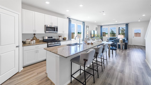 kitchen with visible vents, light stone countertops, a kitchen island with sink, stainless steel appliances, and a sink