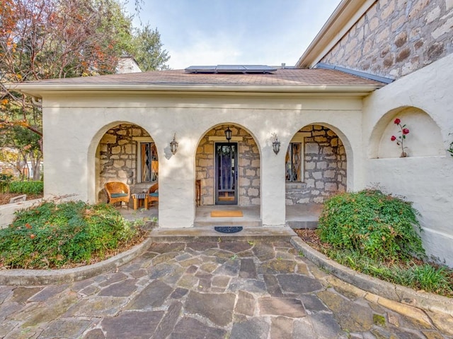 view of exterior entry featuring stone siding, a porch, solar panels, and stucco siding