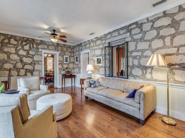 living area with ornamental molding, wood finished floors, visible vents, and baseboards