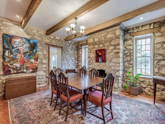 dining space featuring a notable chandelier, a fireplace, wood finished floors, beam ceiling, and crown molding