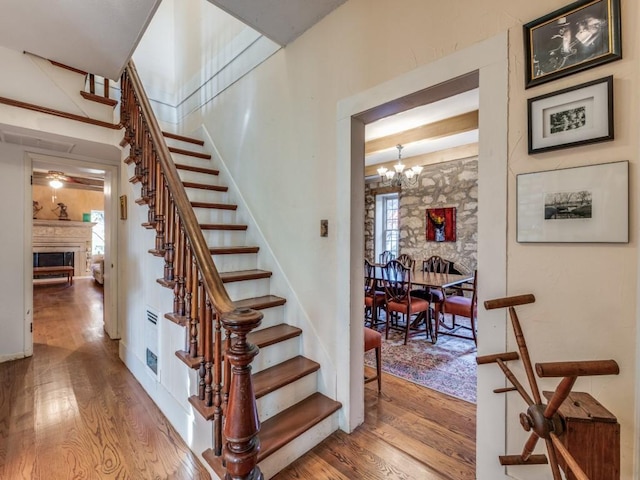 stairs with a notable chandelier, a fireplace, and wood finished floors