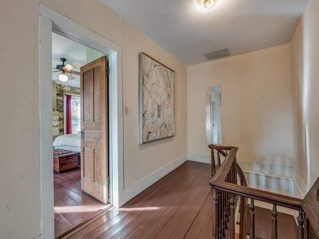 corridor featuring wood-type flooring, visible vents, baseboards, and an upstairs landing