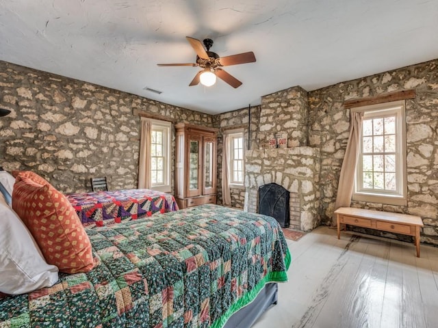 bedroom with hardwood / wood-style flooring, a fireplace, visible vents, and a ceiling fan