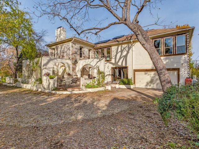 view of front of home featuring dirt driveway, a chimney, stucco siding, and roof mounted solar panels