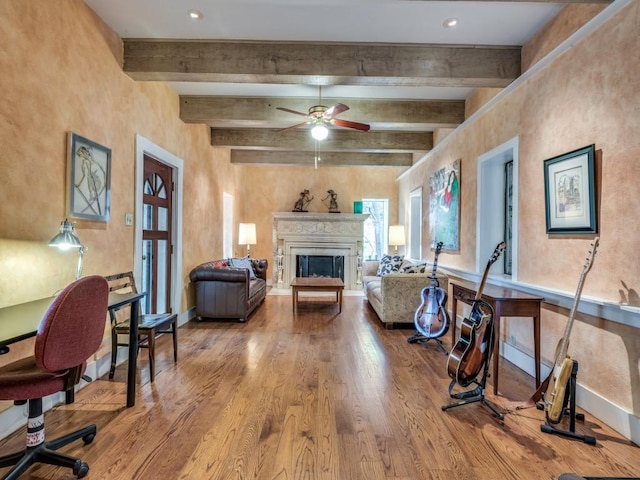 living room featuring a fireplace, wood finished floors, a ceiling fan, baseboards, and beam ceiling