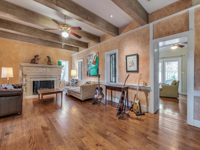 living room featuring ceiling fan, beamed ceiling, a fireplace, and wood finished floors