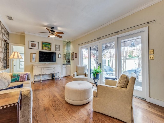 living area featuring visible vents, ornamental molding, a ceiling fan, wood finished floors, and baseboards