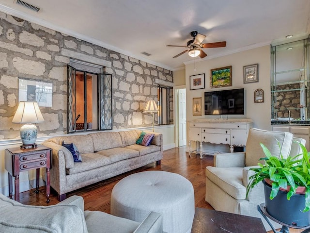 living area featuring a ceiling fan, visible vents, crown molding, and wood finished floors