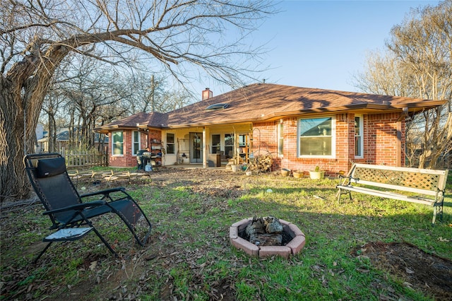 back of property with an outdoor fire pit, a lawn, a chimney, fence, and brick siding