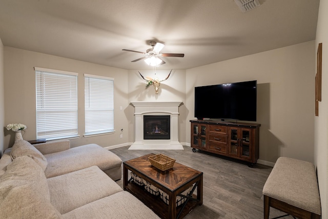 living room featuring visible vents, a glass covered fireplace, ceiling fan, wood finished floors, and baseboards