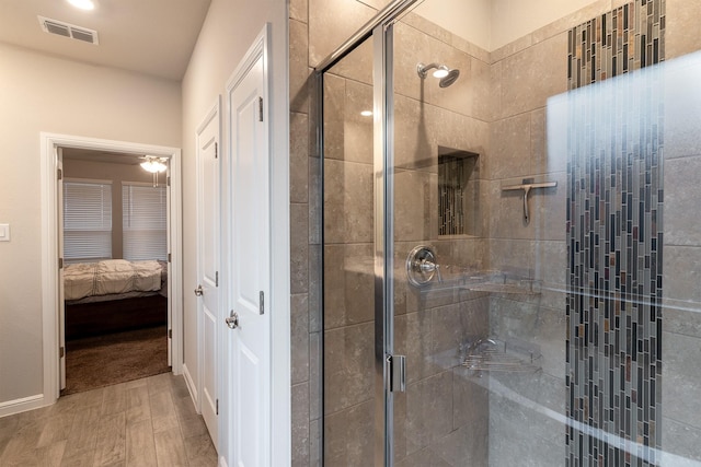 ensuite bathroom with wood finished floors, a shower stall, visible vents, and baseboards