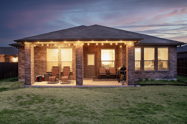 back of property featuring a shingled roof, a lawn, fence, a patio area, and brick siding