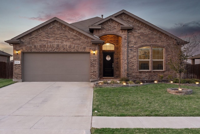 french country inspired facade with a garage, concrete driveway, brick siding, and a yard