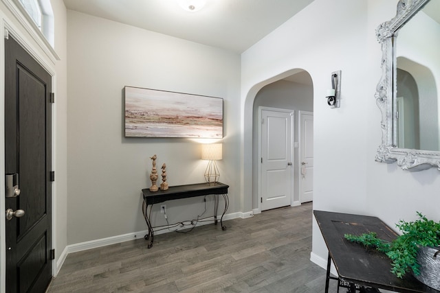 foyer featuring baseboards, arched walkways, and wood finished floors