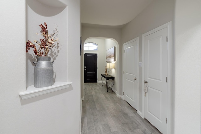 hallway with arched walkways, light wood-style flooring, and baseboards