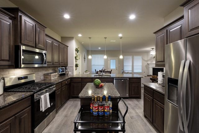 kitchen featuring appliances with stainless steel finishes, a peninsula, a sink, dark brown cabinets, and backsplash