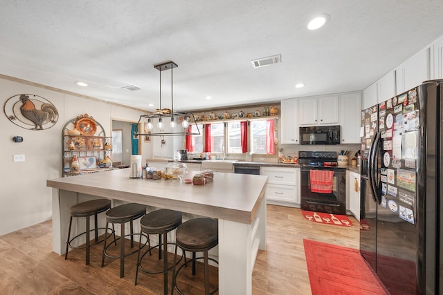 kitchen featuring light wood-type flooring, white cabinets, visible vents, and black appliances